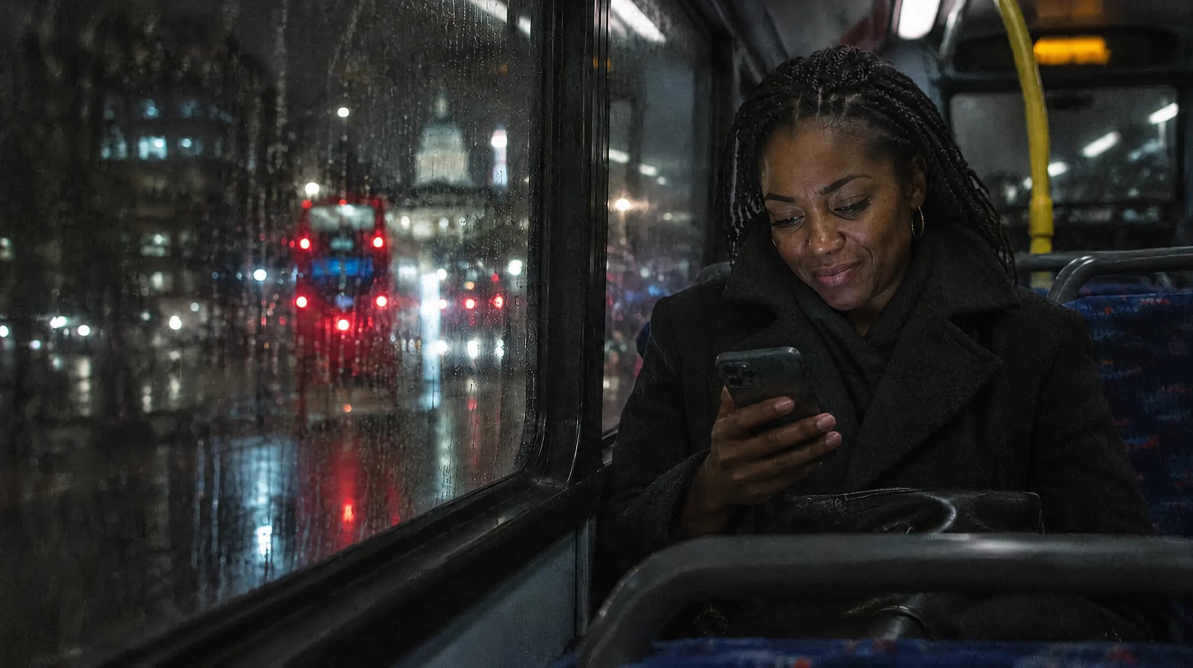 A woman on a London night bus smiling as she reads a message on her phone