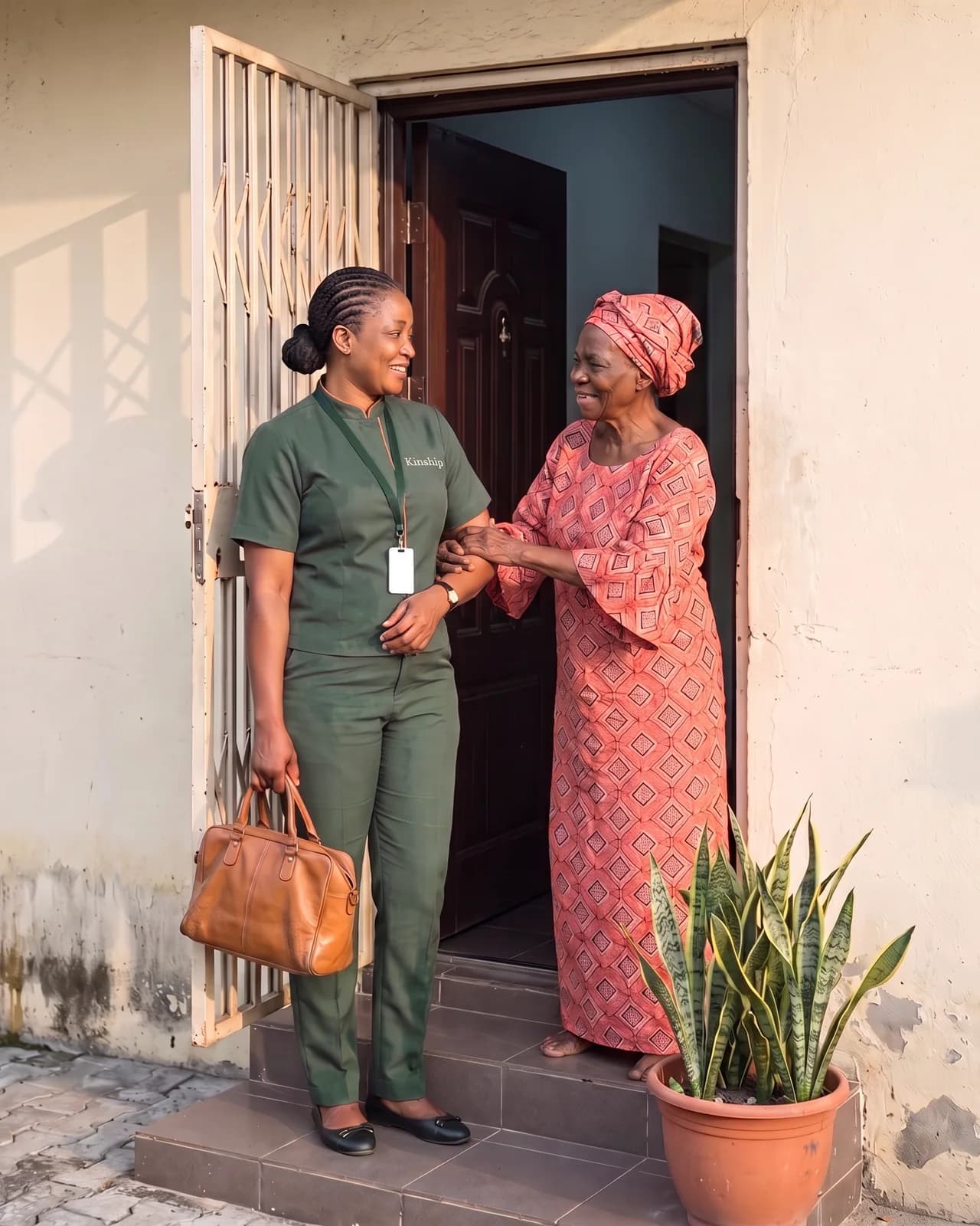 A Kinship nurse in dark green with orange trim greeting an older woman at her front door in Surulere, Lagos